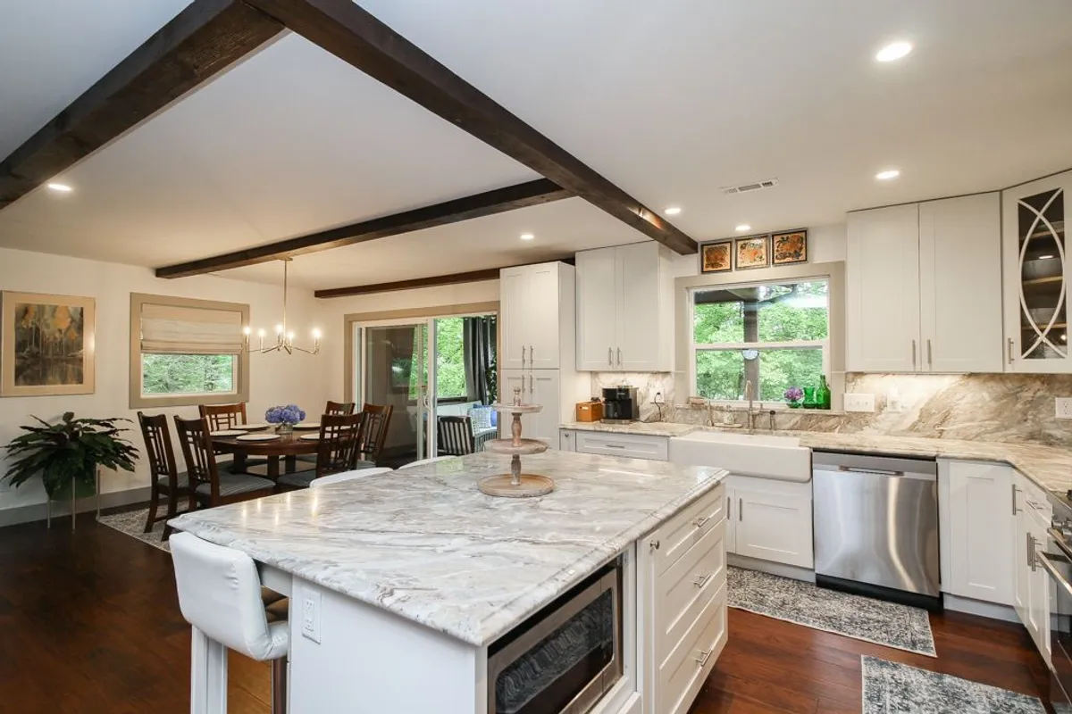 An airy, open kitchen with a prominent kitchen island, a sturdy dining table, and a large window letting in natural light. The space is staged for cooking, entertaining, and gathering—reflecting the heart of culinary activity at Dolly Woods.