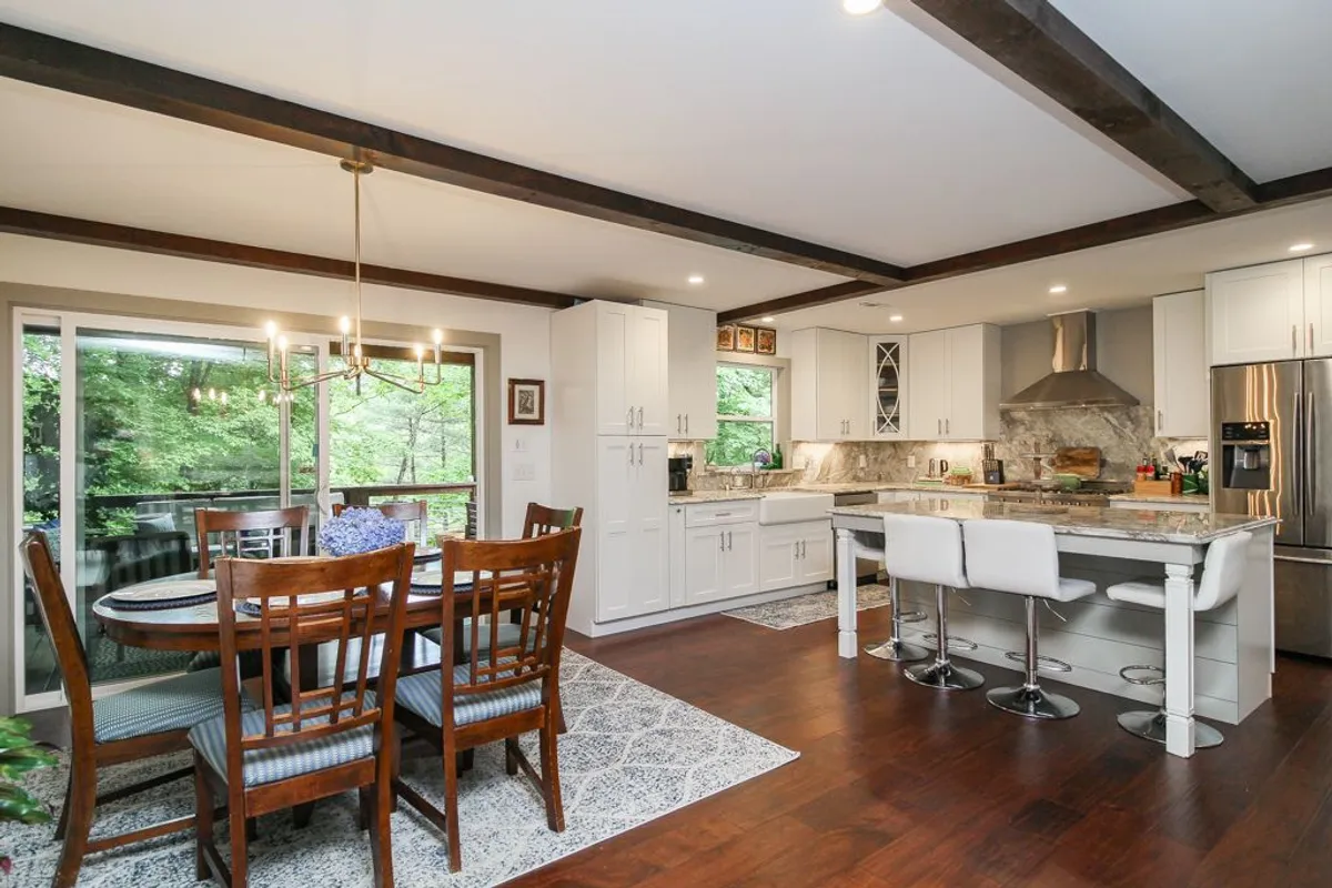 This image shows a bright, open-plan kitchen and dining area with a large kitchen island, a spacious dining table, and large windows that overlook the surrounding natural scenery. The layout invites communal cooking and shared meals, with the island as a central gathering spot.