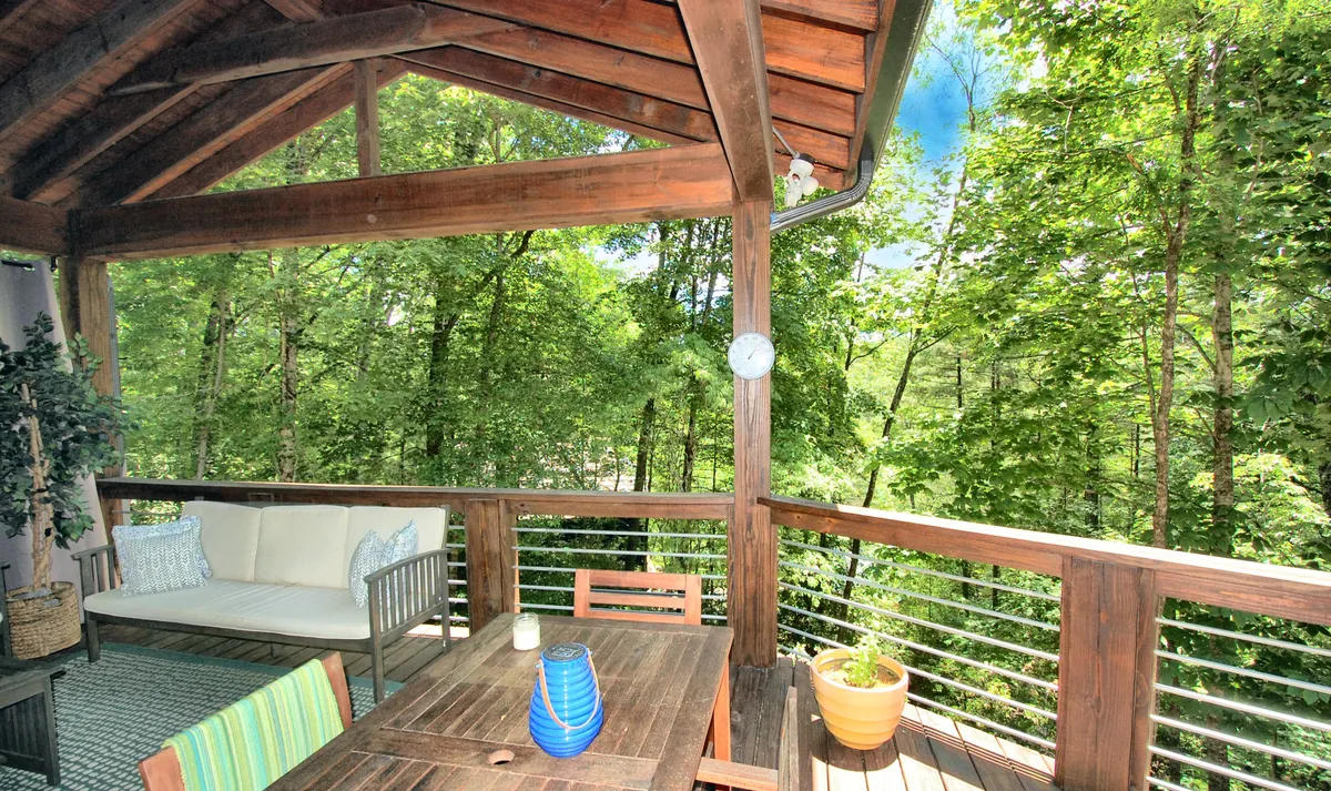 A wooden deck with an outdoor seating area, dining table, and lush green surroundings. The scene is tranquil, with opportunities for morning coffee, reading, or social gatherings while immersed in nature.