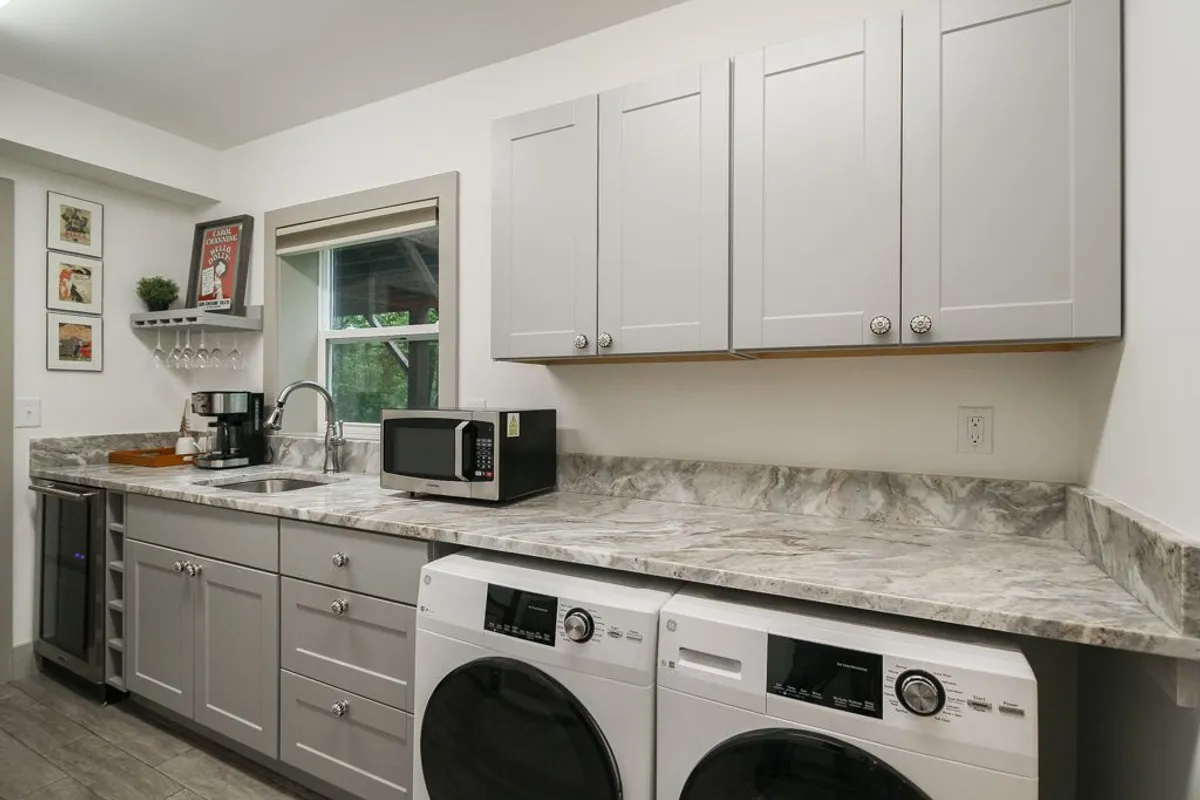 A compact kitchenette with a countertop, coffee maker, microwave, and laundry area. The space is efficient and functional, providing everything guests need for preparing snacks or handling laundry tasks. Framed art adds a touch of personality to the practical setting.