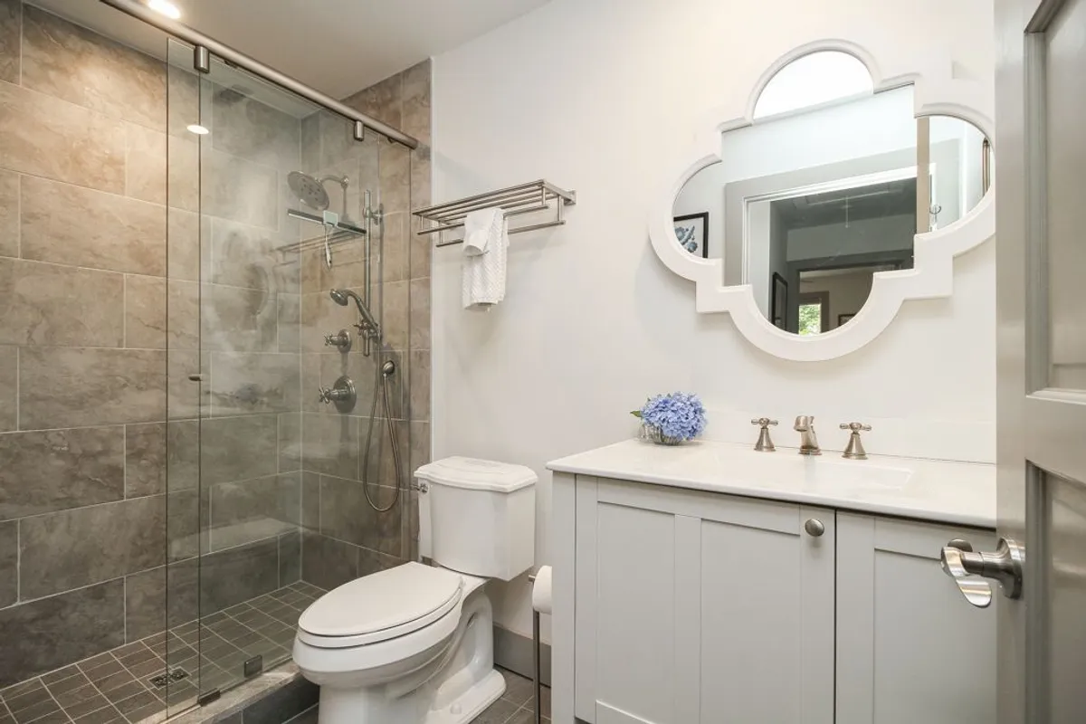 A stylish bathroom interior with a glass shower enclosure, modern vanity with sink, decorative mirror, and a vase of blue hydrangea. The space feels calm, clean, and spa-like, offering a sense of refreshment and comfort.