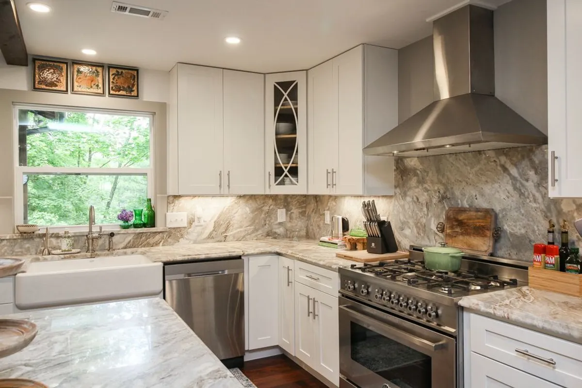 A stylish kitchen with a sleek marble countertop, stainless steel appliances (including a stove), and a large window offering views of greenery outside. The scene captures the gourmet appeal and functional elegance of the kitchen space.