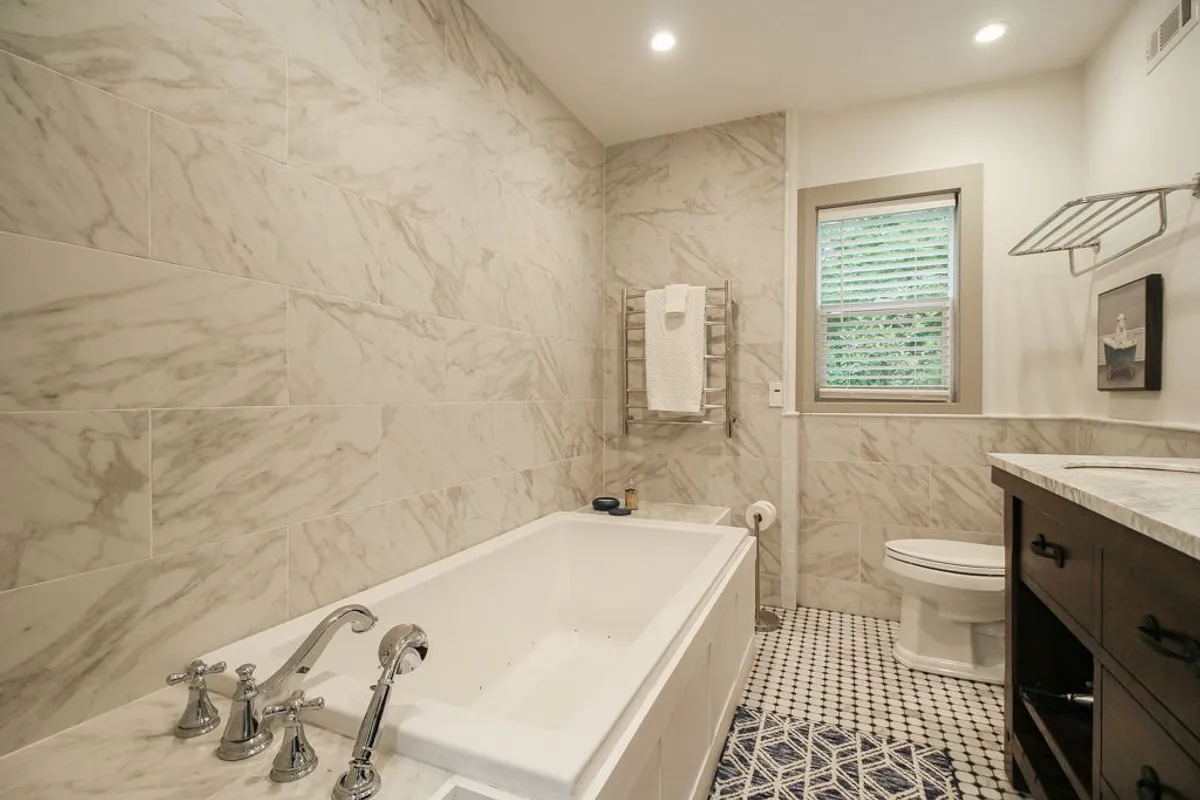 A tranquil bathroom scene with a bathtub, sink, toilet, and neatly arranged towel rack. The space feels serene and soothing, ideal for relaxing after a long day or enjoying a luxurious soak.