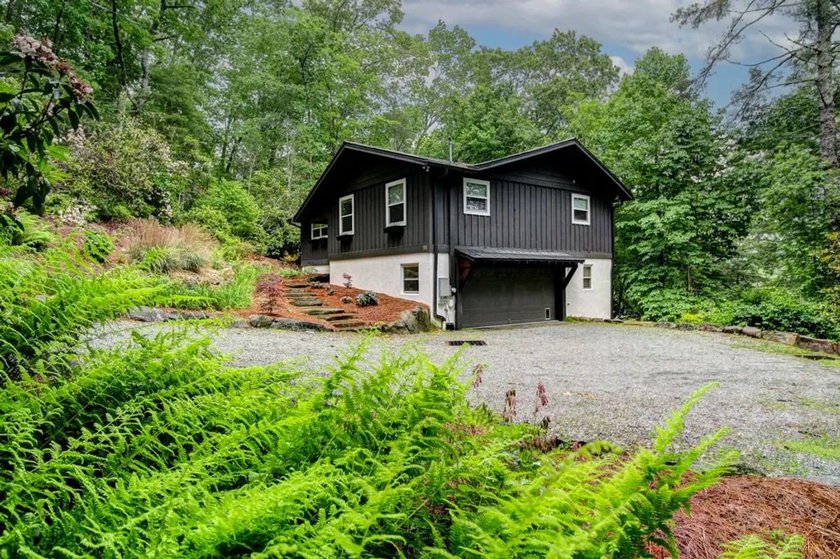 This image captures the home's modern exterior nestled among lush greenery, with a gravel driveway leading up to the entrance. The peaceful, natural setting hints at both relaxation and opportunities for outdoor exploration, perfectly matching the mountain retreat vibe.
