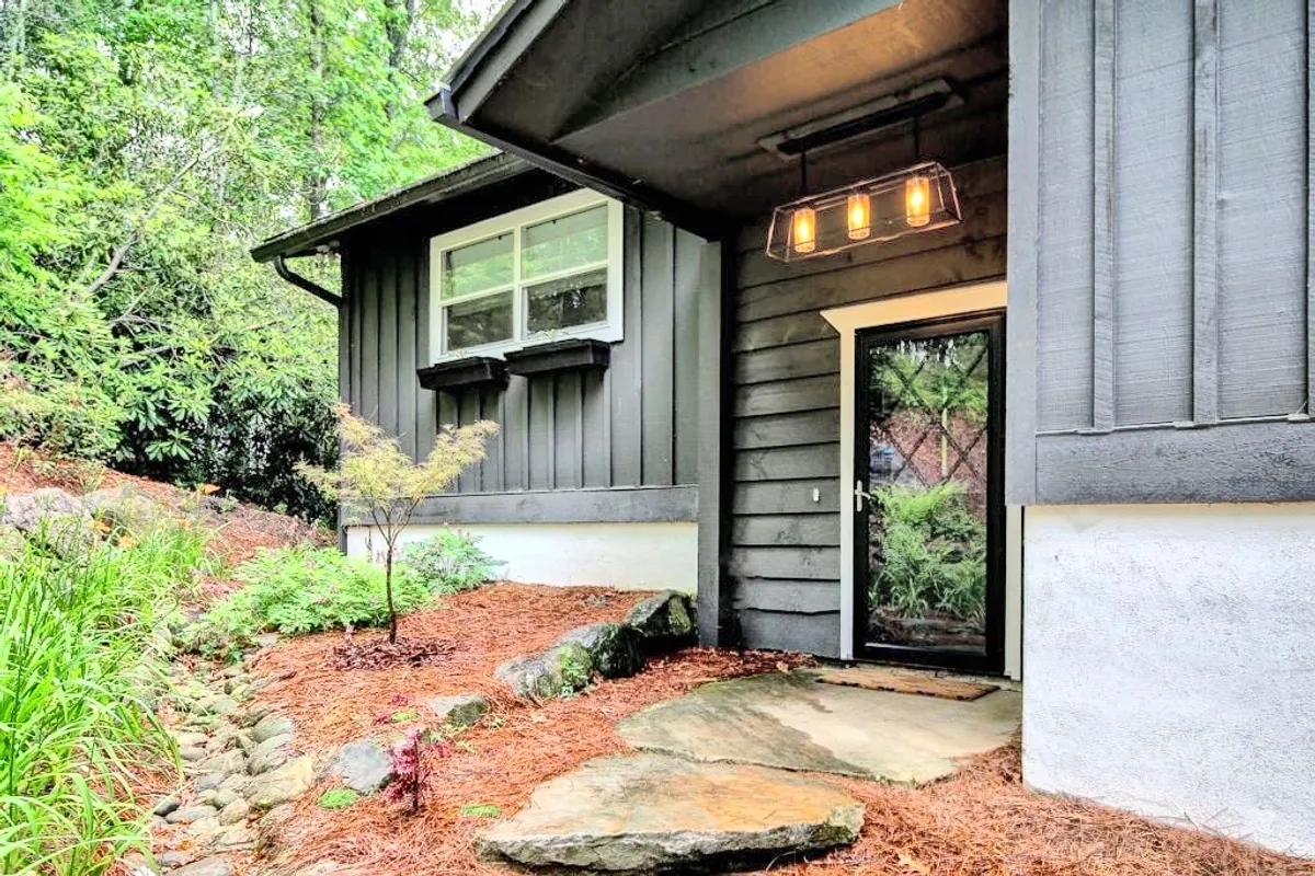 This image captures the inviting front exterior of Dolly Woods, with a charming front door, a classic hanging light fixture, and a winding stone pathway framed by lush greenery. The scene evokes a sense of arrival and the promise of a welcoming retreat after a day spent exploring Highlands' culinary delights.